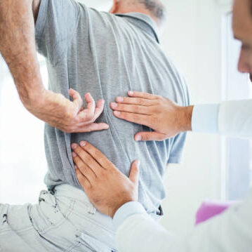 Closeup rear low angle view of an early 60's senior gentleman having some back pain. He's at doctor's office having medical examination by a male doctor. The patient is pointing to his lumbar region.